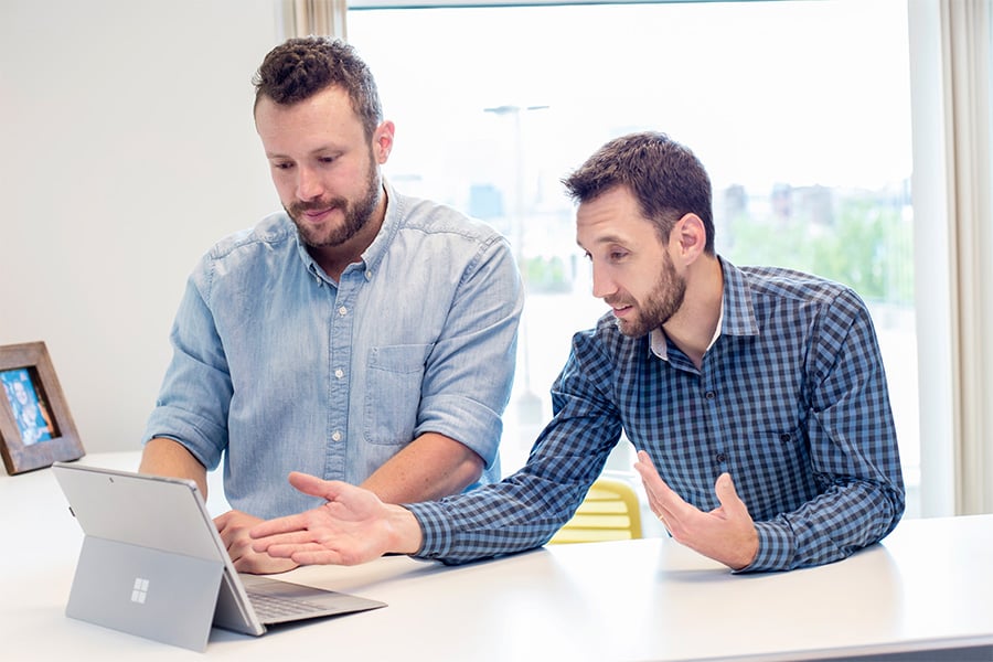 Client-Center-Two-Team-Members-Talking-and-Discussing-in-the-Office-While-Pointing-to-the-Laptop-Sitting-on-the-Desk